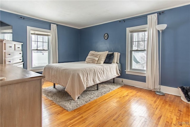 bedroom with ornamental molding, multiple windows, light wood-style floors, and baseboards