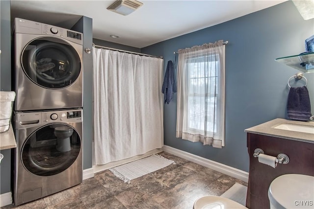 laundry area featuring laundry area, stacked washer / dryer, a sink, visible vents, and baseboards