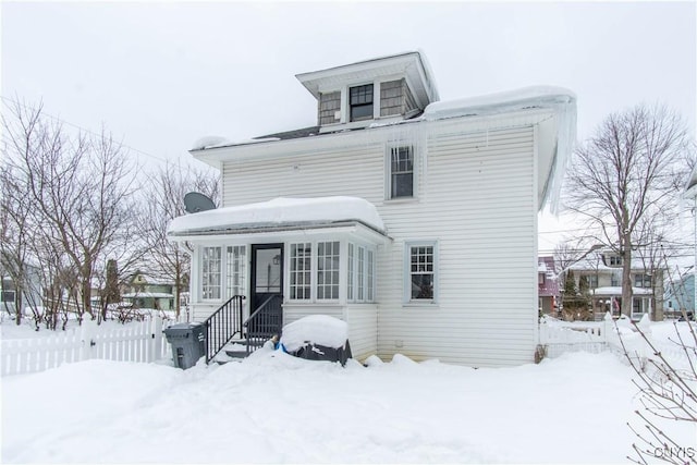 snow covered rear of property with entry steps and fence