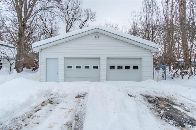 snow covered garage featuring a garage and fence