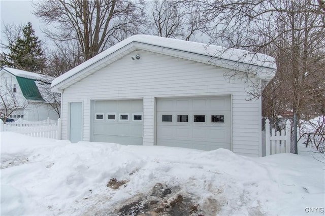 snow covered garage featuring a detached garage and fence