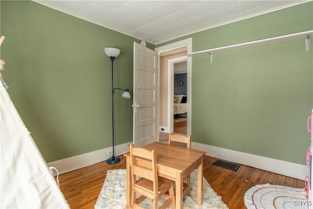 interior space with baseboards, visible vents, wood finished floors, and ornamental molding