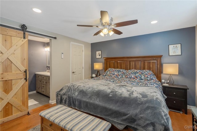 bedroom featuring recessed lighting, light wood-style flooring, a barn door, a sink, and baseboards