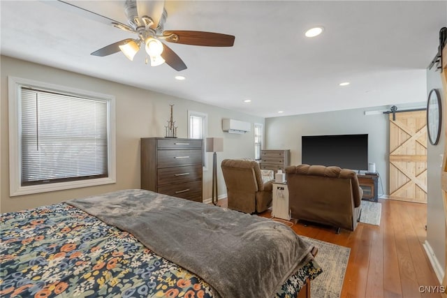 bedroom with a barn door, a ceiling fan, an AC wall unit, light wood-style floors, and recessed lighting