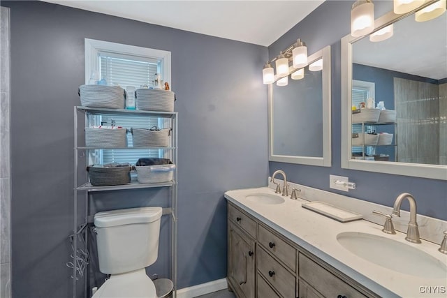 full bath with toilet, double vanity, baseboards, and a sink