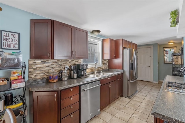 kitchen with light tile patterned floors, stainless steel appliances, a sink, decorative backsplash, and dark countertops