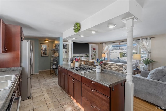 kitchen with stainless steel appliances, open floor plan, reddish brown cabinets, dark countertops, and ornate columns