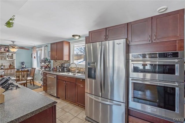 kitchen featuring stainless steel appliances, dark countertops, backsplash, light tile patterned flooring, and a sink