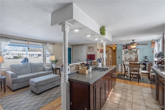 kitchen with dark countertops, dark brown cabinetry, decorative columns, and open floor plan