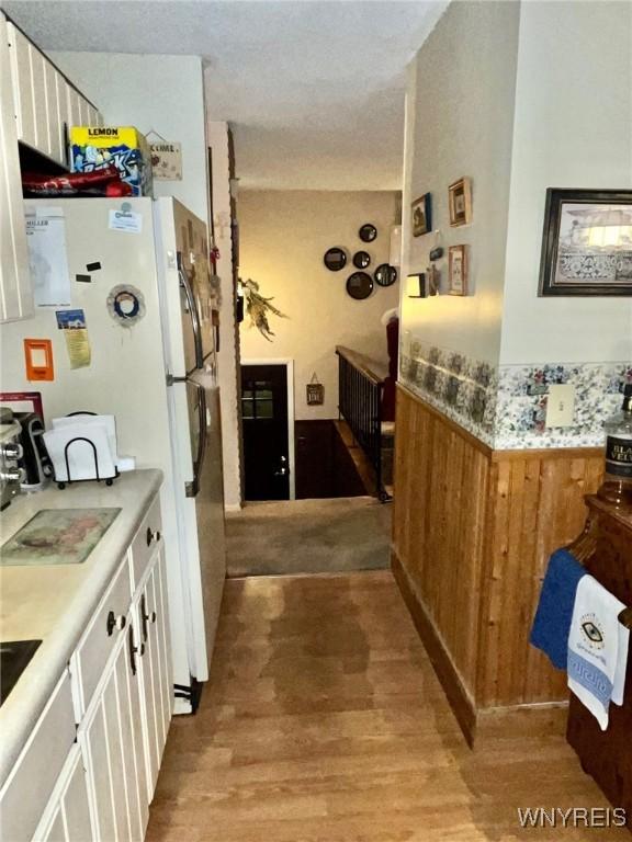 interior space with brown cabinetry, a wainscoted wall, light wood-style flooring, freestanding refrigerator, and light countertops