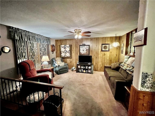 living area featuring wood walls, carpet, a ceiling fan, and a textured ceiling