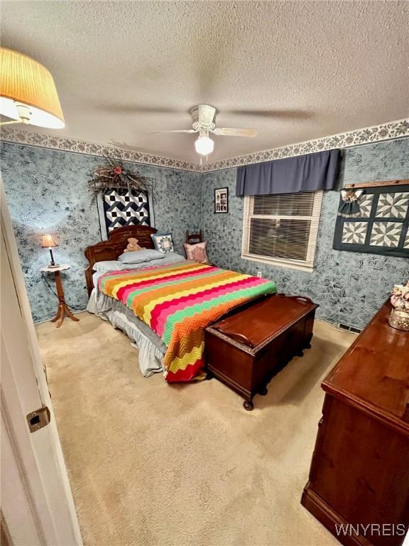 carpeted bedroom featuring a textured ceiling, ceiling fan, and wallpapered walls