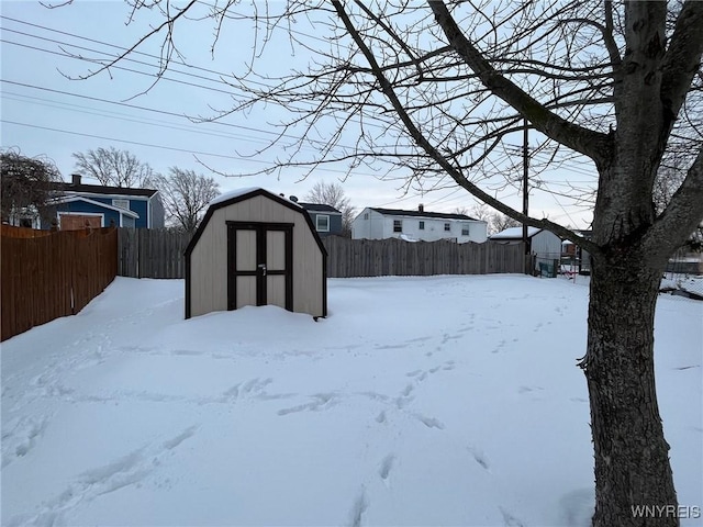 yard layered in snow with a fenced backyard, an outdoor structure, and a storage shed