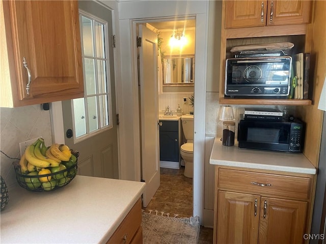 kitchen with light countertops, decorative backsplash, brown cabinetry, a sink, and black microwave