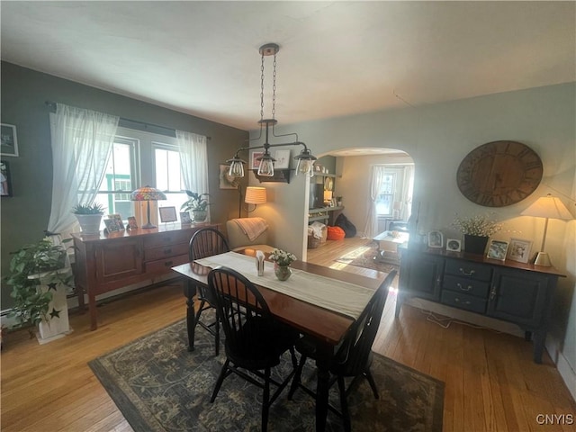 dining area featuring light wood-type flooring and arched walkways