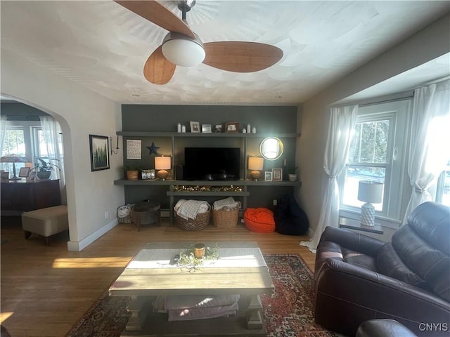 living area with a ceiling fan, baseboards, arched walkways, and wood finished floors