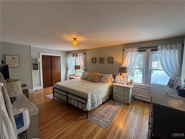 bedroom featuring baseboards, multiple windows, baseboard heating, and light wood-style floors