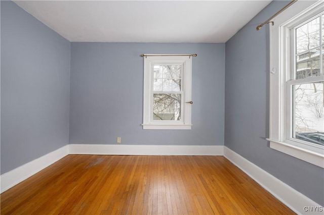 spare room with baseboards, wood finished floors, and a healthy amount of sunlight