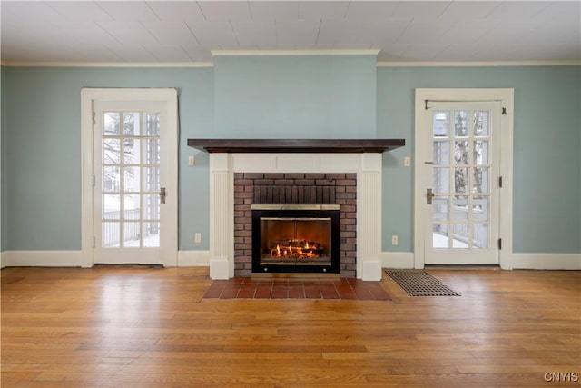 unfurnished living room with baseboards, a brick fireplace, wood finished floors, and crown molding