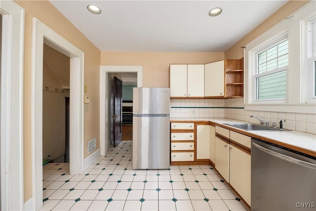 kitchen featuring tile counters, stainless steel appliances, light floors, open shelves, and a sink