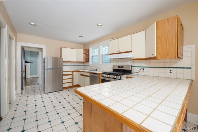 kitchen with tile countertops, under cabinet range hood, appliances with stainless steel finishes, and white cabinets