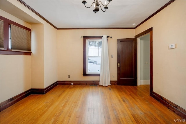 empty room with a notable chandelier, ornamental molding, wood finished floors, and baseboards