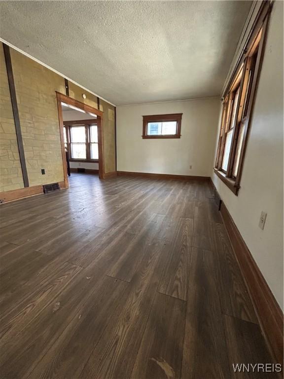 unfurnished living room featuring visible vents, baseboards, dark wood finished floors, and a textured ceiling