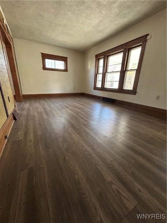 empty room with dark wood-style floors, a textured ceiling, and baseboards