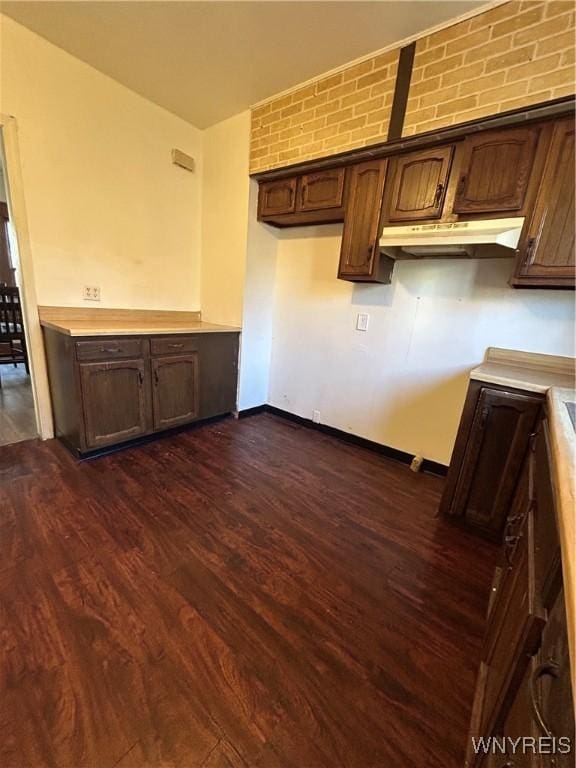 kitchen with light countertops, dark brown cabinets, dark wood finished floors, and under cabinet range hood