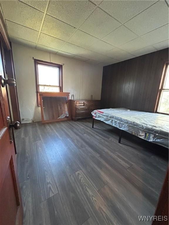 unfurnished bedroom featuring wood walls, dark wood-style flooring, and a drop ceiling