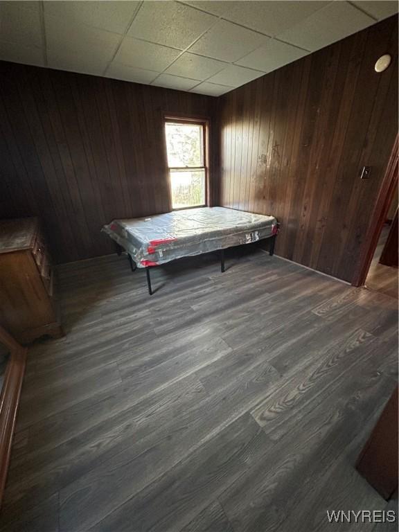 game room featuring dark wood-style floors, a drop ceiling, and wood walls