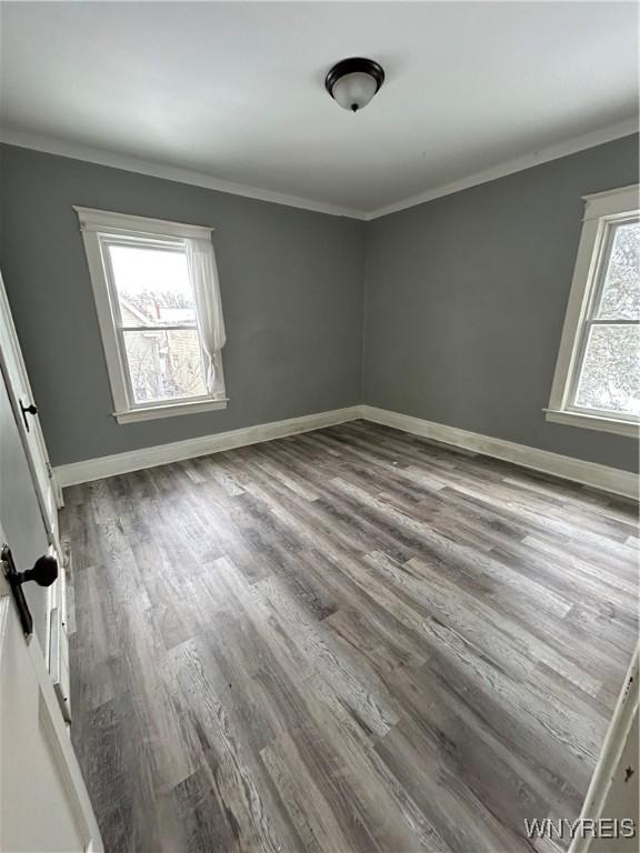 empty room with ornamental molding, wood finished floors, and baseboards