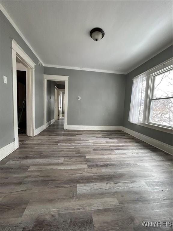 empty room featuring ornamental molding, dark wood-type flooring, and baseboards