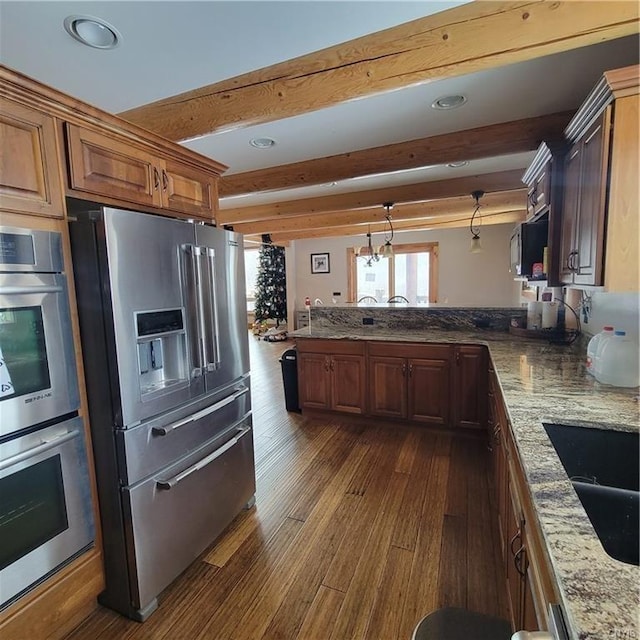 kitchen featuring brown cabinetry, dark wood-type flooring, stainless steel appliances, and beamed ceiling