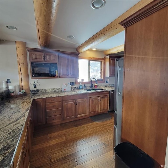 kitchen featuring dark wood-style floors, light stone counters, brown cabinets, a sink, and beam ceiling