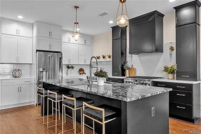 kitchen featuring light wood-style flooring, a kitchen island with sink, wall chimney range hood, range, and decorative light fixtures