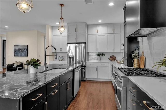 kitchen with premium appliances, pendant lighting, a sink, and wall chimney range hood