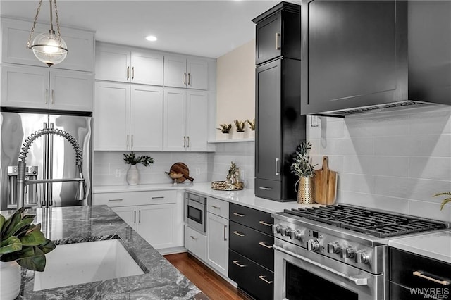 kitchen with white cabinets, dark wood-style floors, appliances with stainless steel finishes, pendant lighting, and backsplash