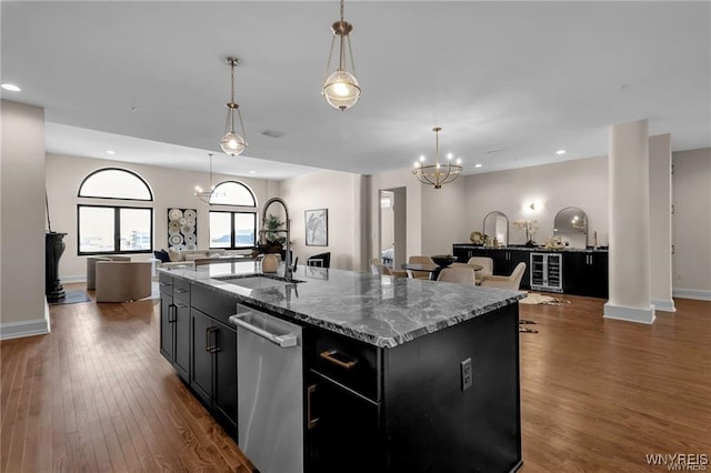 kitchen with stone countertops, a kitchen island with sink, open floor plan, stainless steel dishwasher, and pendant lighting