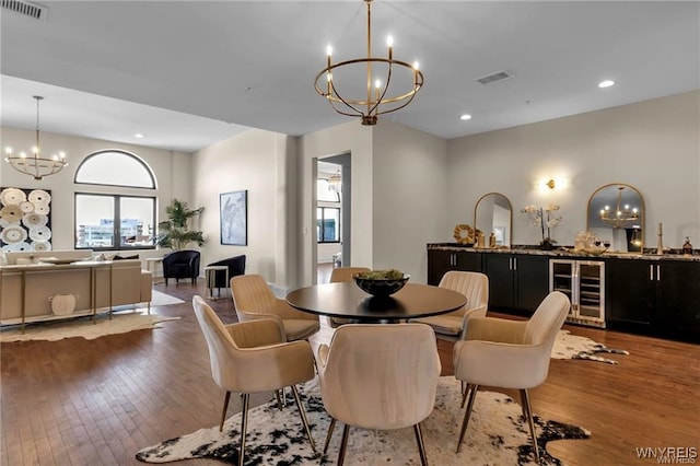 dining space with wine cooler, wood finished floors, visible vents, and a notable chandelier