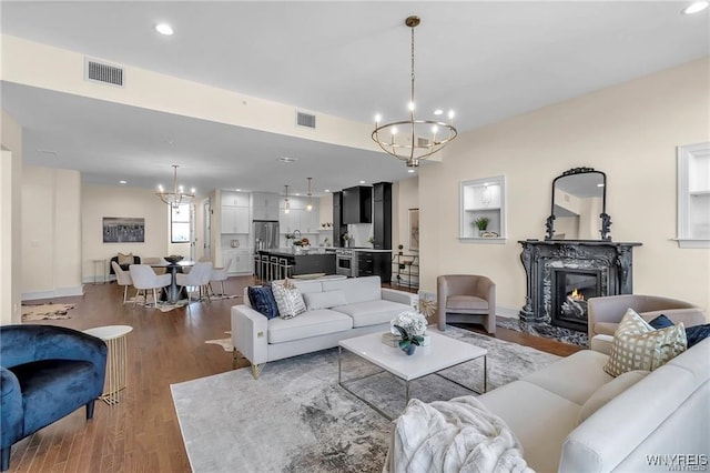 living area featuring wood finished floors, visible vents, a fireplace, and an inviting chandelier