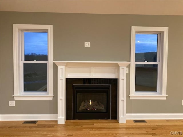 details featuring a warm lit fireplace, visible vents, baseboards, and wood finished floors