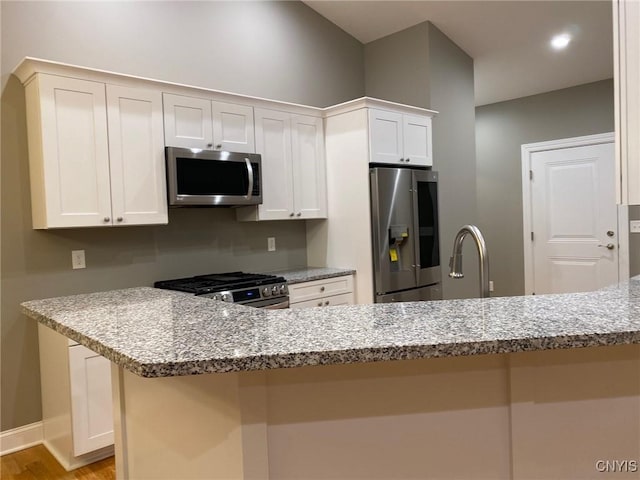 kitchen featuring a breakfast bar area, white cabinetry, stainless steel appliances, and light stone counters