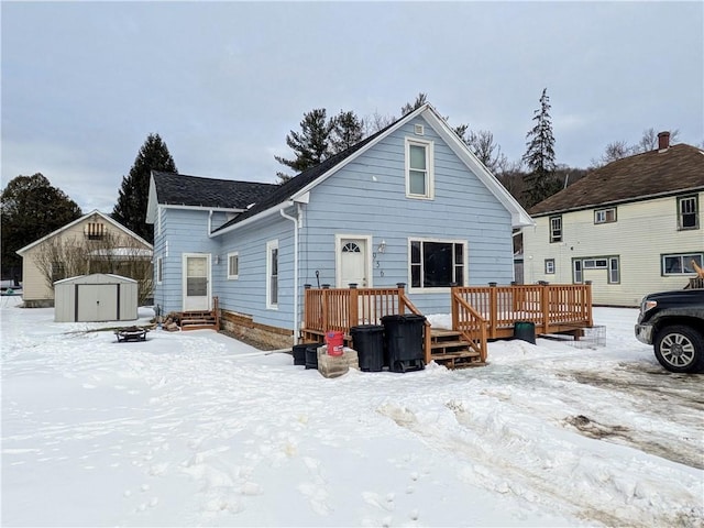 snow covered house with an outbuilding, a wooden deck, and a storage shed