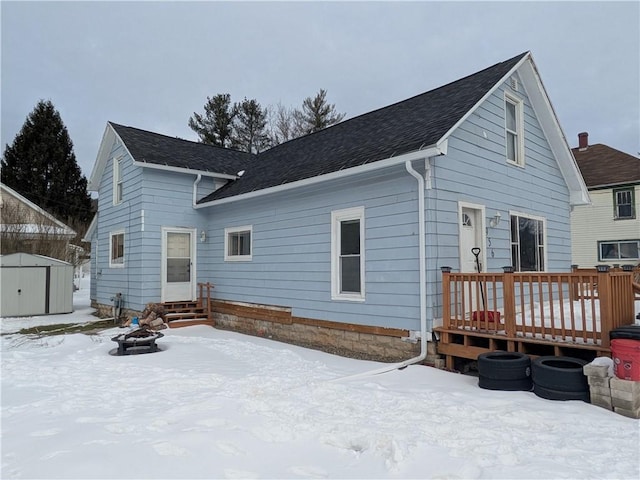 snow covered rear of property featuring entry steps, a fire pit, an outbuilding, a storage unit, and a deck