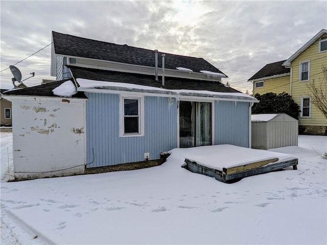 snow covered property with an outbuilding, roof with shingles, and a storage unit