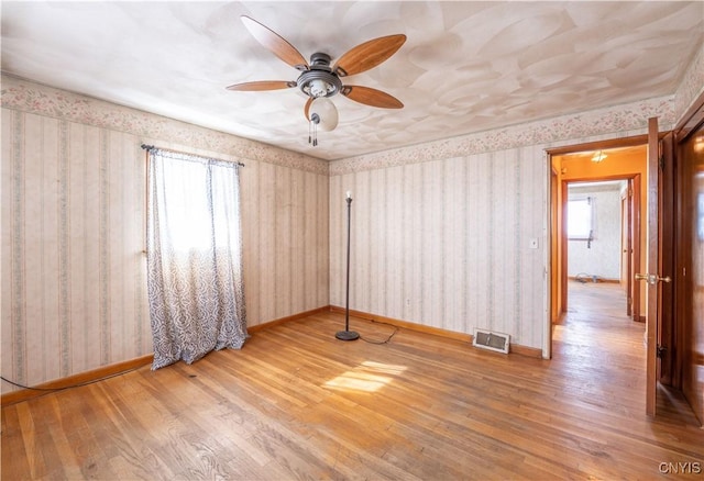 unfurnished room featuring wallpapered walls, baseboards, visible vents, and wood finished floors