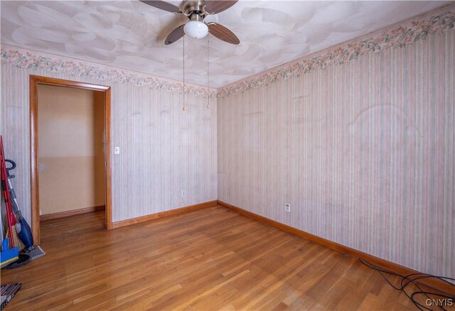 spare room with wallpapered walls, baseboards, and wood finished floors