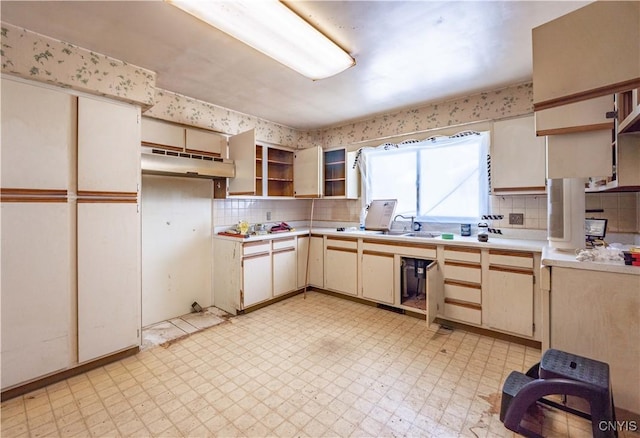 kitchen with glass insert cabinets, light countertops, under cabinet range hood, and light floors