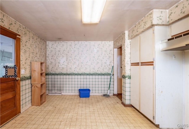 interior space with wallpapered walls, light floors, and wainscoting